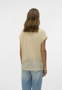 Top de ganchillo beige con un patrón circular, mangas cortas y un corte holgado, combinado con pantalones de mezclilla azul claro.