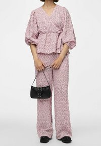 Top peplum con stampa floreale in morbido tessuto rosa, con maniche a palloncino, abbinato a pantaloni coordinati. Tiene una piccola borsa nera con dettagli a fibbia.
