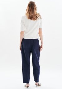 Jasny, krótki sweterek z rękawami do łokci w połączeniu z ciemnoniebieskimi, szerokimi spodniami, które mają tylnie kieszenie i luźny krój. W zestawie znajdują się także buty na wysokim obcasie.