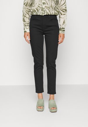 Pantalones negros ajustados con una textura suave, combinados con sandalias de plataforma de ante verdes y una camisa de manga larga con un patrón de motivos de hojas.