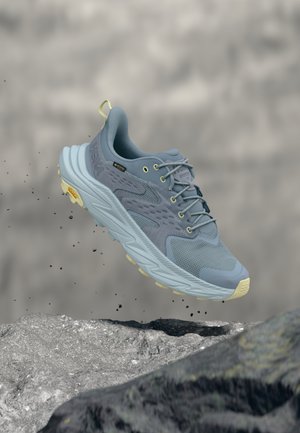 Scarpa da corsa azzurro chiaro con tomaia testurizzata, dettagli verdi e suola ammortizzata. Presenta una suola esterna ad alta aderenza e dettagli riflettenti.