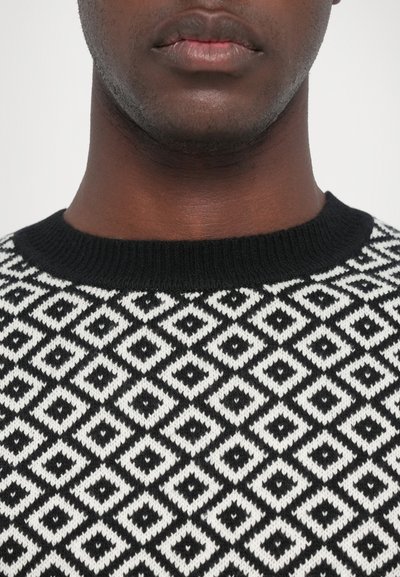 Black and white patterned sweater featuring a diamond design, knitted texture, and a black ribbed crew neckline.