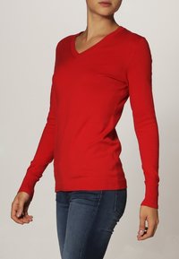 Pull à manches longues rouge en V, design ajusté, poignets et ourlet côtelés, fabriqué en tissu tricoté lisse, idéal pour le superposition.