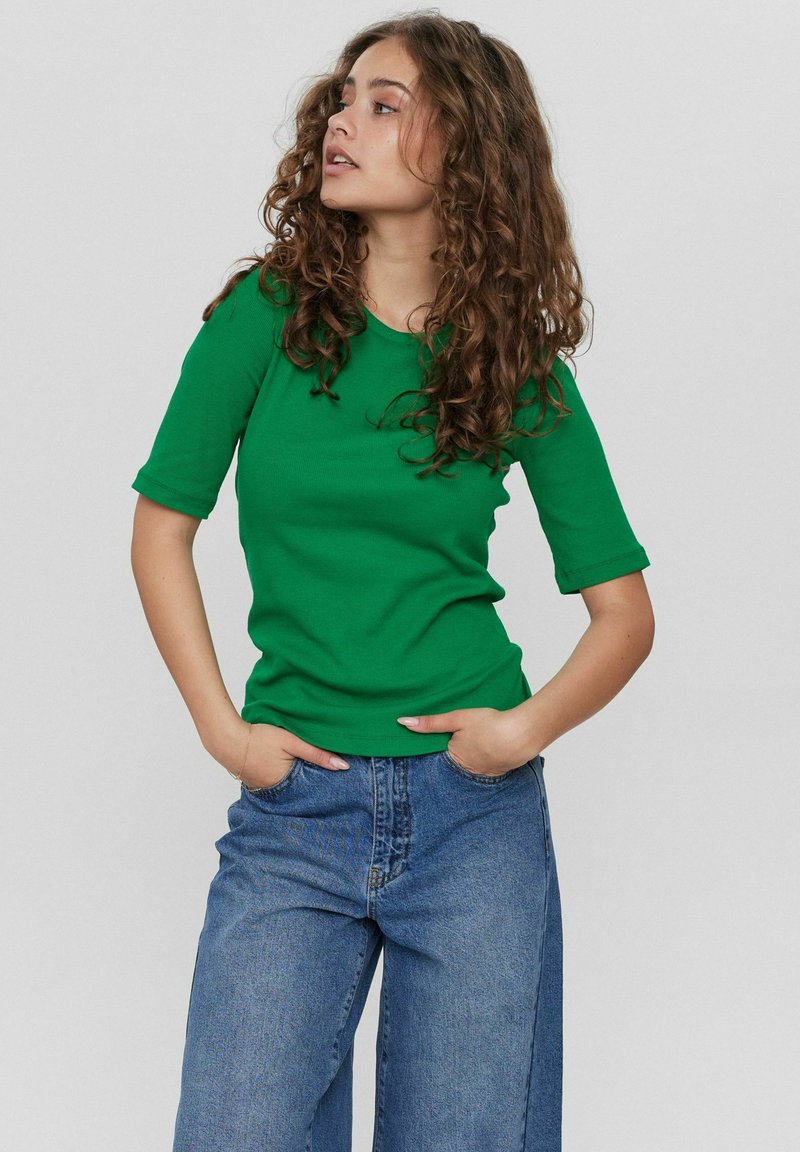 Groene geribde t-shirt met korte mouwen, gecombineerd met losse blauwe denim broek. De stof lijkt zacht en textuurrijk.