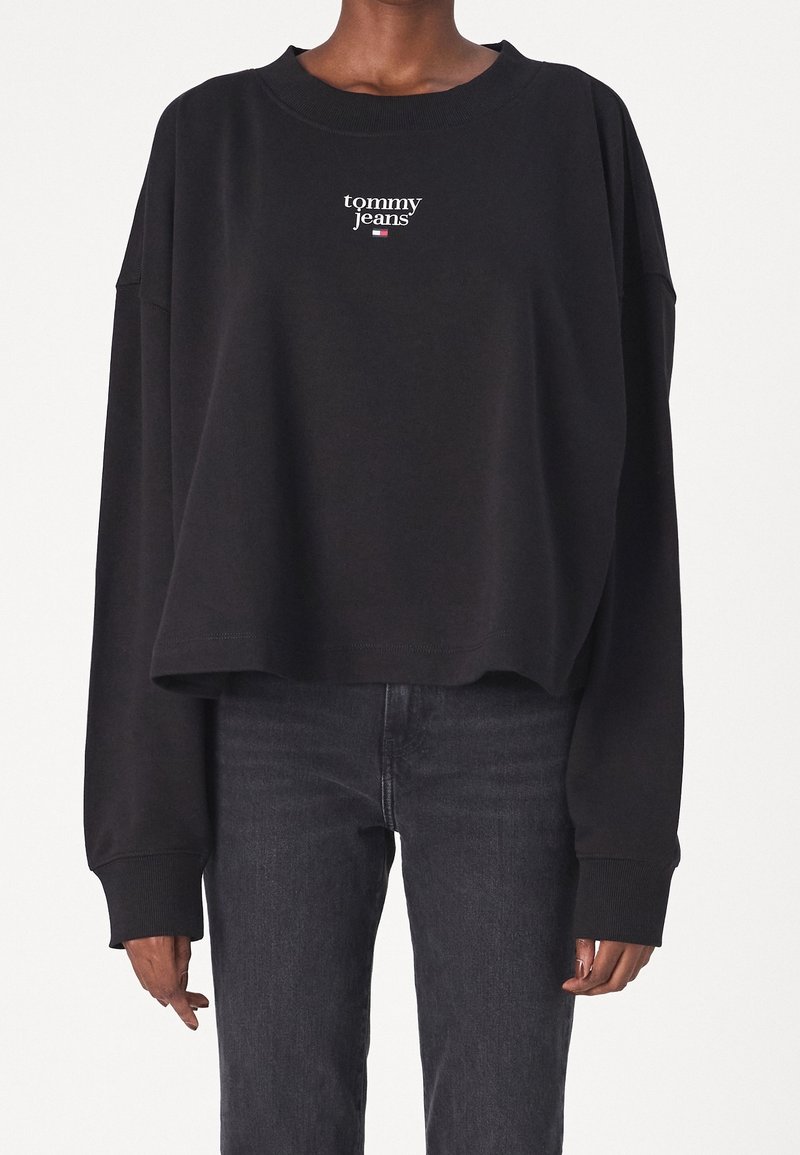 Felpa nera con un design cropped e maniche lunghe. Presenta un logo bianco "tommy jeans" sul petto. Il materiale sembra morbido.
