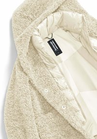 Beiger, flauschiger Oberstoff mit strukturiertem Finish, gefüttert mit glattem, cremefarbenem Material; verfügt über eine Kapuze und dezente Druckknopfverschlüsse.
