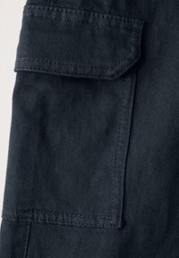 Mørkeblå stof med en lomme med klap, synlige sømme og en glat tekstur. Fokus på funktionelt design og materialets kvalitet.