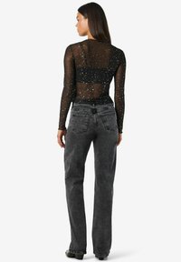 Črn prozoren top z dolgimi rokavi in zlatimi pikami, v kombinaciji z visokim pasom temno sivo širokima hlačami. Vidna šivanka in žepi.