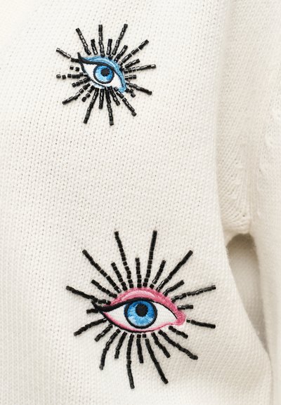 Λευκό πλεκτό  ύφασμα με δύο κεντημένα σχέδια ματιών. Το ένα μάτι είναι μπλε και μαύρο, το άλλο ροζ και μπλε, και τα δύο με ακτινωτές μαύρες λεπτομέρειες.