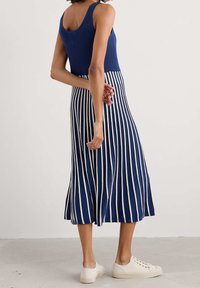 Robe midi rayée bleu marine et blanche avec un design débardeur côtelé, tissu texturé, et jupe évasée. Associée à des baskets de couleur claire.