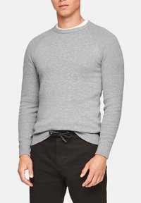 Šedý pletený svetr s kulatým výstřihem a žebrovanou texturou, v kombinaci s černými kalhotami a šňůrkou v pase. Jednoduchý a funkční design.