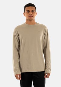 T-shirt a maniche lunghe beige realizzato in tessuto morbido, con collo rotondo, polsini aderenti e un piccolo logo sul petto.