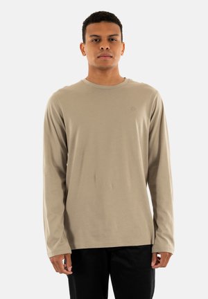 Camiseta de manga larga de color beige, hecha de una tela suave, con cuello redondo, puños ajustados y un pequeño logo en el pecho.