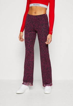 Hoge taille uitlopende broek van donker stof met een roze abstract patroon, voorzien van een zachte structuur en een franjeszoom. Draagt met witte sneakers.