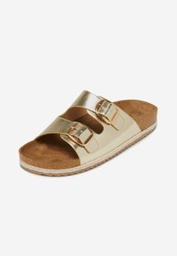 Gouden metallic sandalen met twee verstelbare gespen, een zachte bruine gevoerde binnenzool en een gestructureerde rubberen zool. Heeft een plat ontwerp.