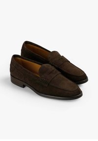 Mocasines de ante marrón con un detalle de costura en el empeine y un tacón bajo y suave. Presentan una punta redondeada y una textura suave.