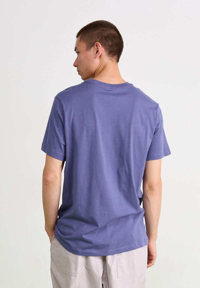 Camiseta de manga corta y cuello redondo en tela de algodón de color púrpura claro, con un diseño liso y un pequeño detalle de dobladillo en la parte posterior.