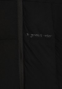Svart puffjakke med jevn overflate, som har hel glidelås og en subtil "Originals Studio"-logo på brystet.