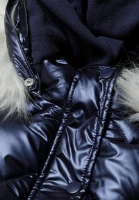 Námořnická puffer bunda s lesklou, prošívanou látkou, vystavenou umělou kožešinou a černými knoflíky. Měkká, texturovaná podšívka viditelná.