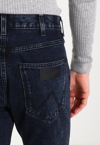 Mörkblå denimjeans med en läderetikett från Wrangler på bakfickan, med klassisk passform och subtil textur.