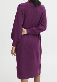 Abito a maglia viola a maniche lunghe, a coste, con corpetto aderente, spacchi laterali e silhouette rilassata, caratterizzato da maniche a palloncino e scollo rotondo.