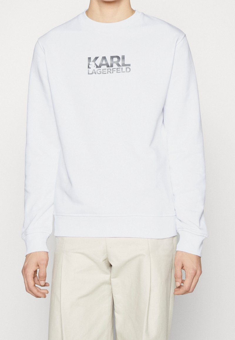 Weißer Sweatshirt aus weichem Stoff mit Rundhals. Mit silbernem Logo-Text "KARL LAGERFELD" auf der Vorderseite und gerippten Bündchen.