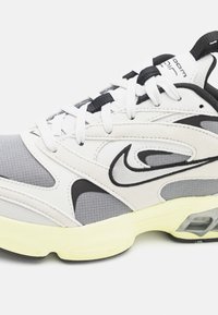 White and gray sneaker with mesh and suede materials. Black accents, thick sole with visible air unit, and white laces. Simple logo detail.