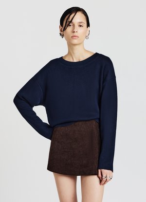 Maglione in maglia blu navy con scollo ampio e maniche lunghe abbinato a una minigonna in velluto a coste marrone con strisce verticali.