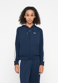Sweat à zip bleu marine en tissu doux, avec des rayures blanches sur les côtés et un cordon de serrage ajustable, doté d'une finition côtelée au poignet et à l'ourlet.