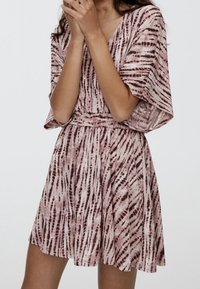 Short-sleeve pink dress with a v-neck, featuring a smocked waist and a tie-dye pattern of maroon stripes, made from lightweight fabric.