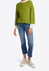 Groen gebreide trui met een losse pasvorm, lange mouwen, gecombineerd met cropped blauwe spijkerbroeken en beige hoge sneakers. Getextureerde, casual look.