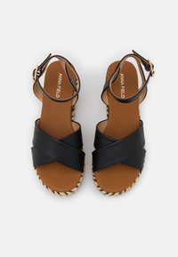 Černé espadrilové sandály s křížovým designem, hnědou vložkou z umělé kůže a tkanou podešví podobnou jutu. Nastavitelný nártový pásek s sponou.