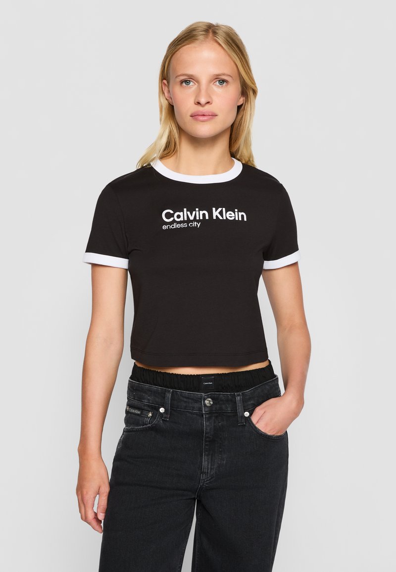 Juoda trumpa marškinė su balta kontrastine apykakle ir rankogaliais, su užrašu "Calvin Klein" ir "endless city" išspausdintu ryškiomis baltomis raidėmis.