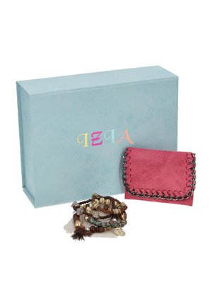 Cartera rosa adornada con una cadena y varios brazaletes de cuentas, expuestos delante de una caja de regalo azul claro con la marca.