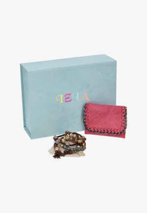 Cartera rosa adornada con una cadena y varios brazaletes de cuentas, expuestos delante de una caja de regalo azul claro con la marca.