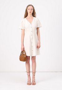 Beige linnen jurk met een V-hals, korte pofmouwen en een sluiting met knopen aan de voorkant. Gekocht met een geweven bruine handtas en bandjesandalen.
