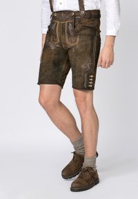 Bruna lederhosen i mocka, med dekorativ broderier, hängslen och utsmyckade knappar på sidan. I kombination med bruna stövlar och grå strumpor.