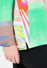 Top colorido de manga corta con patrones abstractos en verde, rosa, naranja y gris, hecho de una tela suave y texturizada.