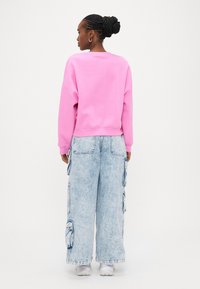 Rosa Sweatshirt mit lockerem Schnitt und gerippten Bündchen, kombiniert mit hellblauen, weit geschnittenen Cargo-Jeans mit Seitentaschen, getragen mit weißen Sneakers.