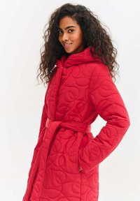 Czerwona pikowana kurtka z kapturem, paskiem w talii i ozdobnymi wzorami liści. Miękka w dotyku i o luźnym kroju dla wygody.
