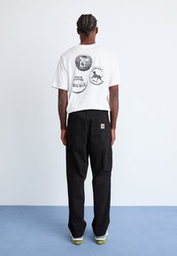 White graphic t-shirt with circular prints and text, paired with black cargo pants featuring multiple pockets. Casual, relaxed fit.
