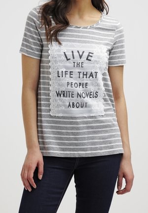 Kvinde iført en grå og hvid stribet T-shirt med korte ærmer, blonder og tekst, der lyder "Live the life that people write novels about."