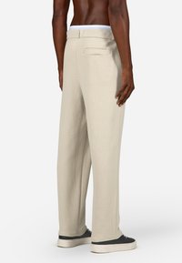 Bež hrapave hlače z ohlapnim krojem, ki imajo bel pas in zadnji žep. V kombinaciji z črnimi športnimi copati, ki poudarjajo kontrast.