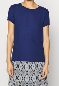 T-shirt blu navy a maniche corte con scollatura rotonda, tessuto morbido e maniche arrotolate, abbinato a una gonna fantasiosa con motivi a diamante e floreali.