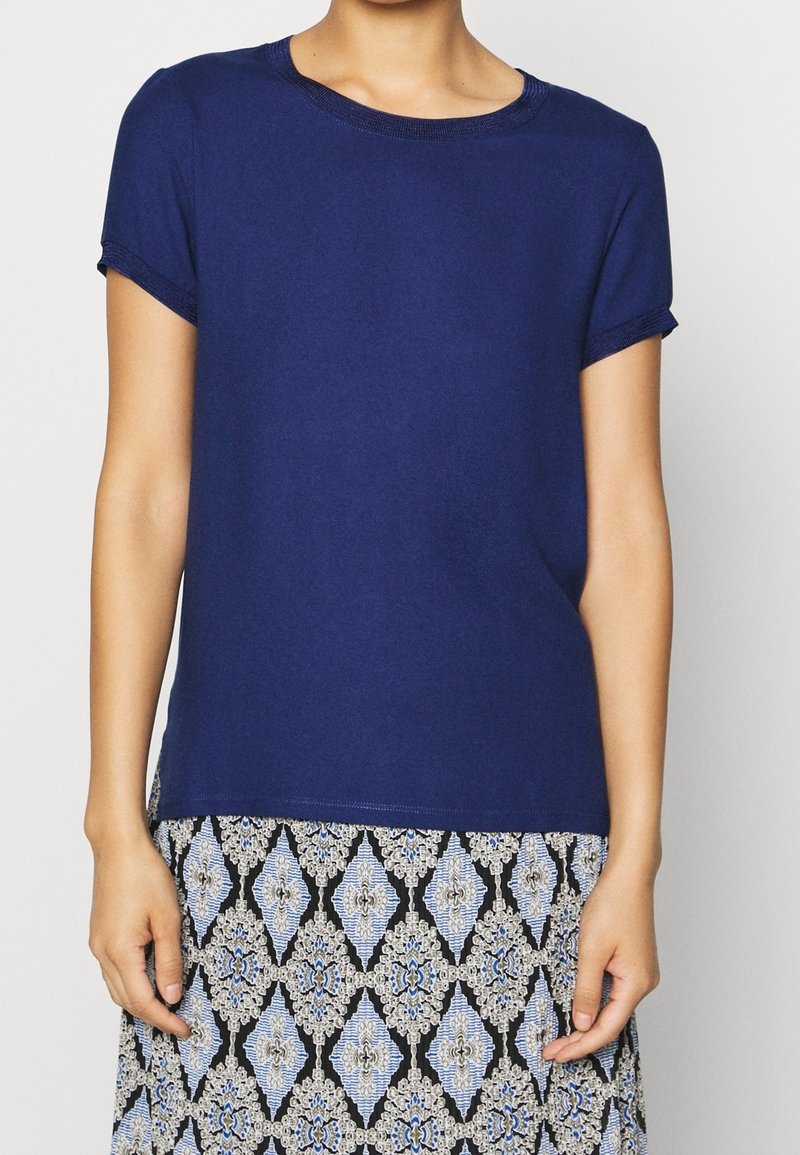 T-shirt blu navy a maniche corte con scollatura rotonda, tessuto morbido e maniche arrotolate, abbinato a una gonna fantasiosa con motivi a diamante e floreali.