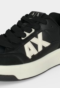 Baskets Armani Exchange noir et blanc avec semelle blanche épaisse, lacets noirs et grand logo blanc "AX" sur le panneau latéral.