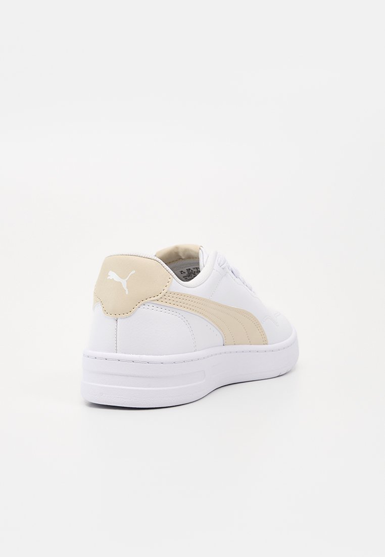 Baskets Puma blanches et beiges vues de dos et de côté, montrant le logo Puma sur la languette du talon et la semelle texturée.
