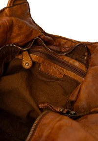 Interieur van een bruine leren tas met een klein ritsvakje met het label "REDESIGNED EST. 2003" en een stoffen voering.