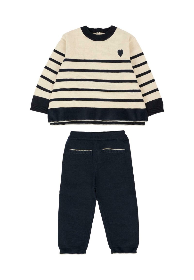 Maglione a righe crema e blu navy con dettaglio a cuore, abbinato a pantaloni blu navy a tinta unita con tasche posteriori decorative e polsini a costine.