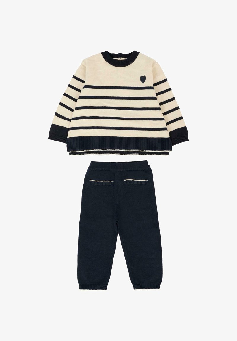 Maglione a righe crema e blu navy con dettaglio a cuore, abbinato a pantaloni blu navy a tinta unita con tasche posteriori decorative e polsini a costine.